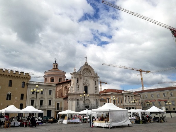 La piazza del Duomo de l'Aquila ha solo qualche impalcatura residua, ma è di nuovo una piazza vera, dove passeggiare, guardare le vetrine e fare il mercato.