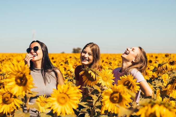 Tre giovani ragazze sorridono in un campo di girasoli: la felicità per la ripresa delle vacanze studio per il 2022?