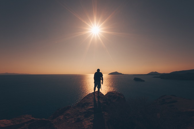 Una ragazzo con lo zaino guarda il tramonto sul mare: le vacanze trekking non offrono solo lunghi cammini.