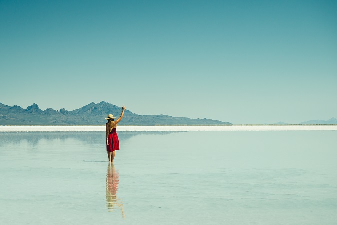 Una ragazza di spalle cammina in un corpo d'acqua, alzando un braccio al cielo in segno di rivincita.