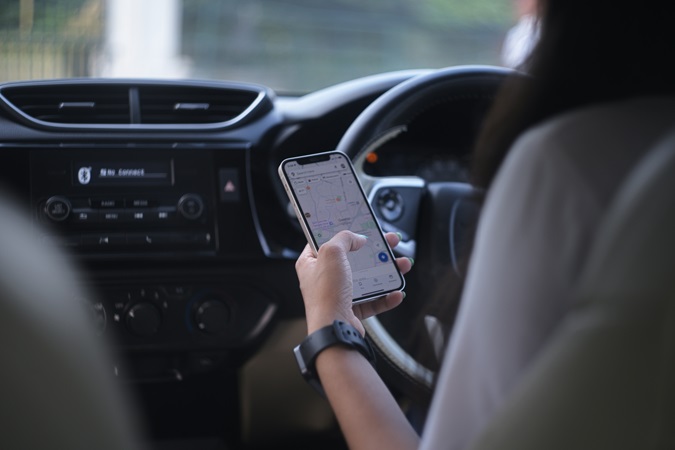 Una donna al volante, con guida a destra, mentre imposta una destinazione sul navigatore del cellulare.
