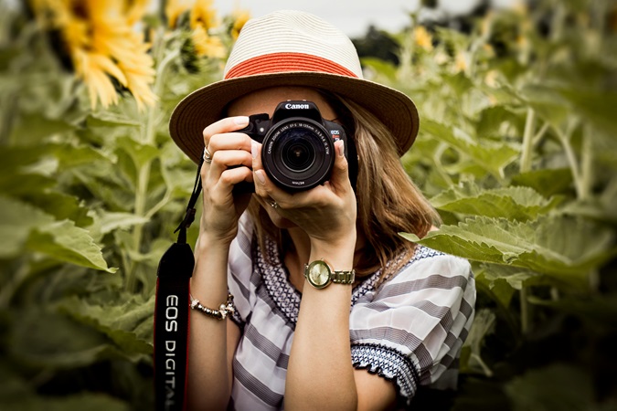 Primo piano di una giovane fotografa con cappello, immersa in un campo di papaveri.
