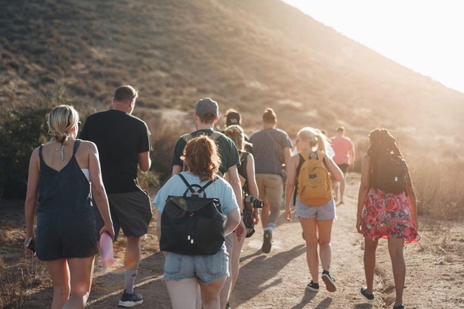 Gruppo di persone in cammino fotografato di spalle. Il cammino è l'invito dell'edizione 2025 del festival Immagimondo.