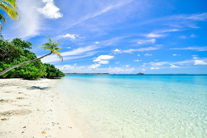 Foto da cartolina delle Maldive: mare cristallino, palme e un'imbarcazione all'orizzonte. Idea per un viaggio a Capodanno 2026.